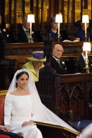 Meghan Markle de noiva. Ao fundo, a rainha e o príncipe Philip