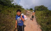 Indígenas Yanomamis caminham em estrada de barro e carregam suprimentos
