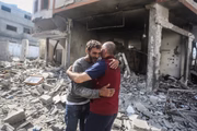 Homens palestinos confortam uns aos outros enquanto inspecionam o bairro devastado de Karama após o bombardeio israelense na Cidade de Gaza
