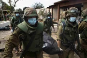 Soldados israelenses removem os corpos de civis, que foram mortos dias antes em um ataque de militantes palestinos neste kibutz perto da fronteira com Gaza