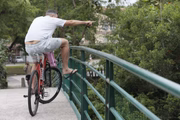 Pai ciclista aponta os jacarés para a filha, na garupa da bicicleta