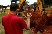 Enquanto a escavadeira joga terra sobre o caixão, em cemitério de Goiânia, familiar de uma das pessoas enterradas reza