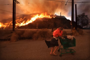 Uma mulher sem-teto empurra seus pertences para fora da Pacific Coast Highway e Topanga Canyon Blvd enquanto o incêndio em Palisades desce as colinas em Pacific Palisades, Califórnia, na terça-feira, 7 de janeiro de 2025