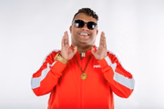 MC Delux posa, sorridente e de moletom vermelho, segurando o colar