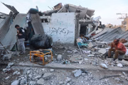 Palestinos sentam-se em frente a uma casa danificada em Khan Yunis, no sul da Faixa de Gaza, em meio às batalhas em curso entre Israel e o grupo palestino Hamas