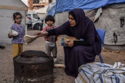 Uma mãe prepara uma refeição para seus filhos do lado de fora de sua casa improvisada em um campo de refugiados em Khan Younis, Gaza.