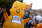 Manifestantes contra o ex-presidente se fantasia de Trump com uma placa escrito "loser", perdedor em inglês