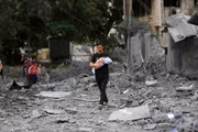 Homem com criança de colo se muda para um local mais seguros em meio a edifícios destruídos e destroços após ataques aéreos 