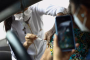 Em Goiânia, enfermeira aplica a dose da vacina e acompanhante do paciente registra o momento
